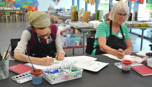 Two participants focusing while painting with watercolor palettes.