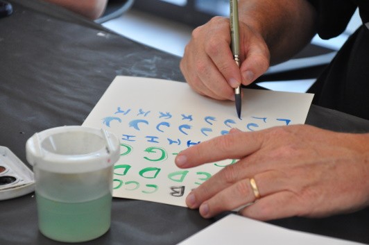 Close-up of a participant painting the alphabet with watercolor and varying their brush strokes.