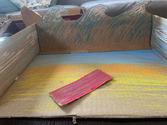 Cardboard waves are added to the back of the cardboard box to create a beach scene. 