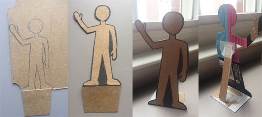 Four images side by side showing the process of a cardboard figure being cut out, standing through the use of a folded tab at the base, and a supporting cardboard rectangle at the back. 