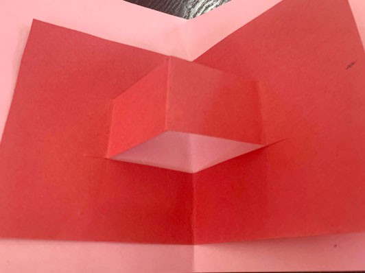 A red, cut-out pop-up nestled into the fold of a pink card.