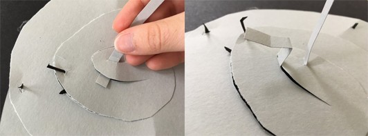 Two images showing a thin piece of grey paper being threaded through a cut in the spiral, then folded to make a paper hook.