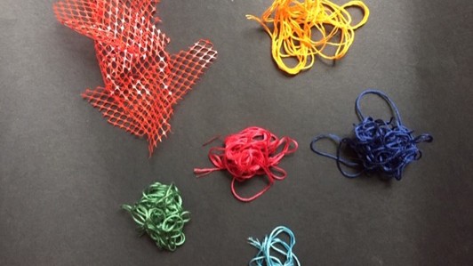 Piles of brightly colored embroidery threads and a pile of orange plastic mesh.