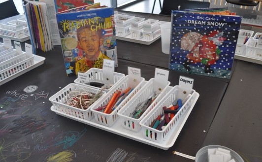The books Radiant Child by Javaka Steptoe and Dream Snow by Eric Carle stand on the table near art materials to inspire guests.
