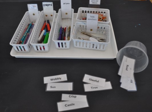 Materials (colored pencils, crayons, gel pens, yarns and ribbons, hole punchers, and word cards are on the table in containers, ready to use.